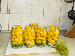 Rows of Homemade Pattypan Squash Preserves in Glass Jars. A row of glass jars containing small yellow pattypan squash stands on a light kitchen surface, accompanied by fresh dill. The composition show © Nadiia