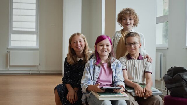 Portrait of Caucasian children smiling at camera holding digital tablet and notebooks in school. Useful for back to school campaigns, edtech marketing, and education promotions