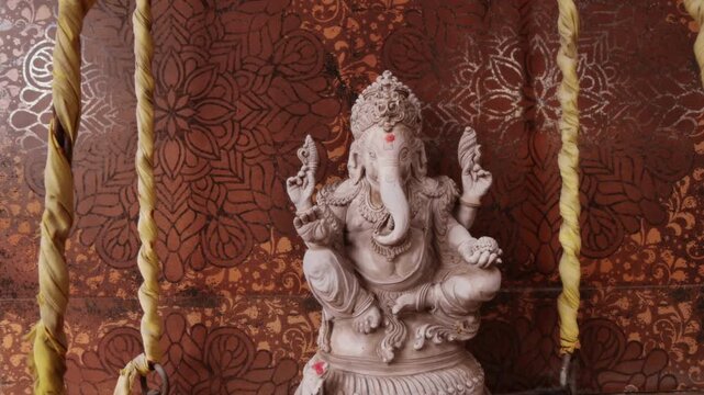 A detailed, light-colored stone statue of Ganesha, seated in a traditional pose with four arms, best for Ganesh chaturthi video