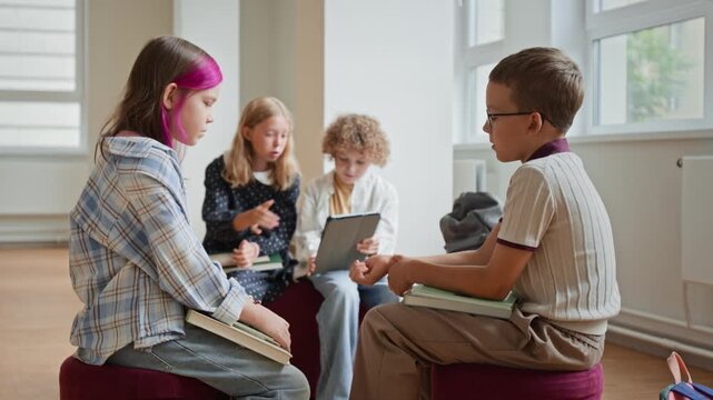 Caucasian children sitting together, discussing school assignment with digital tablet and books. Video represents collaborative modern education, group teamwork, and smart learning