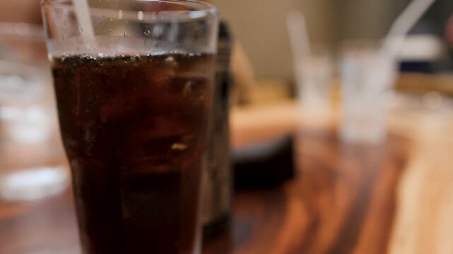 Cold Glass of Cola with Ice Cubes on Wooden Restaurant Table