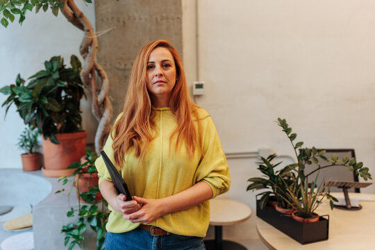 Redhead woman holding tablet standing in modern office