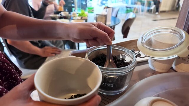 Scooping Dry Tea Leaves Into Ceramic Cup with Metal Spoon