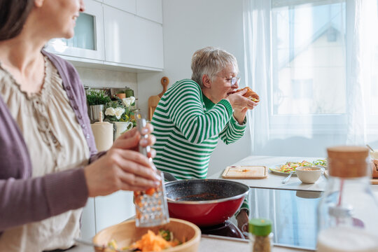 Senior woman enjoying food while cooking with daughter