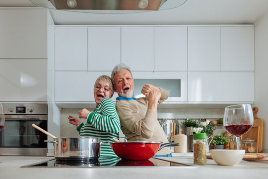 Senior couple having fun dancing cooking in kitchen