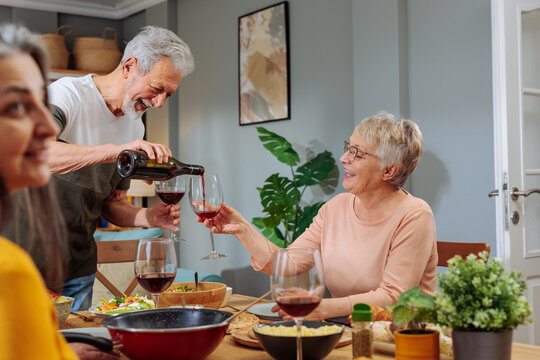 Senior man pouring red wine for happy friends
