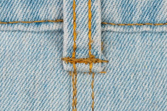 Extreme closeup of light blue denim texture. Detailed macro shot shows classic orange thread, seam and belt loop on jeans. Perfect for fashion, textile, or background concepts