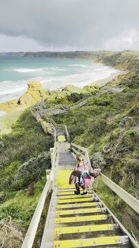 A girl traveler stands on a wooden boardwalk, admiring the stunning rock formations at the beach, Yellow Rock, Portland, Victoria, Australia.