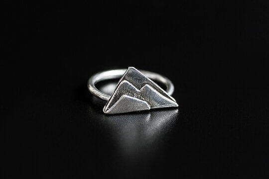 A silver ring featuring a mountain design. The ring has a polished finish and is set against a black background, highlighting its intricate details.