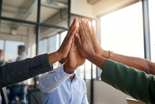 Diverse business colleagues giving a high-five in a sunny modern office, celebrating team success and achievement for human resources and corporate culture marketing.