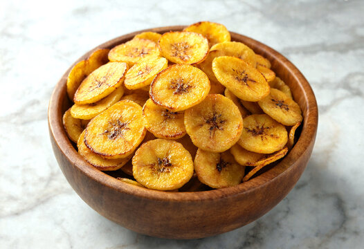 Crispy fried plantain chips served in a wooden bowl on a marble surface for a healthy snack option