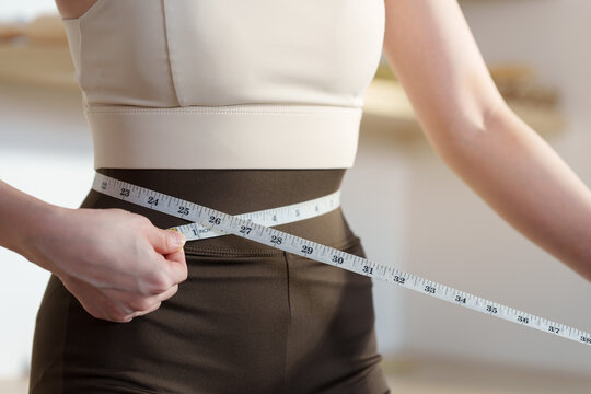 Cropped woman measuring waist with tape measure for fitness progress and body health