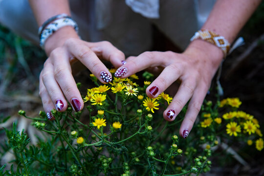 Woman hands touching yellow wildflowers with nail art