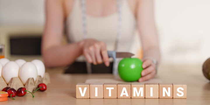 Wooden blocks spelling vitamins with woman slicing green apple for healthy nutrition
