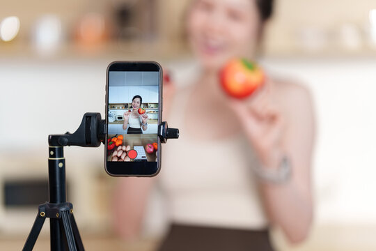 Asian woman recording healthy food vlog video with smartphone in kitchen