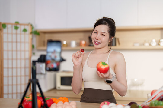 Asian woman vlogging with smartphone on tripod in kitchen about healthy eating