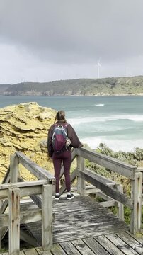 A girl traveler stands on a wooden boardwalk, admiring the stunning rock formations at the beach, Yellow Rock, Portland, Victoria, Australia.