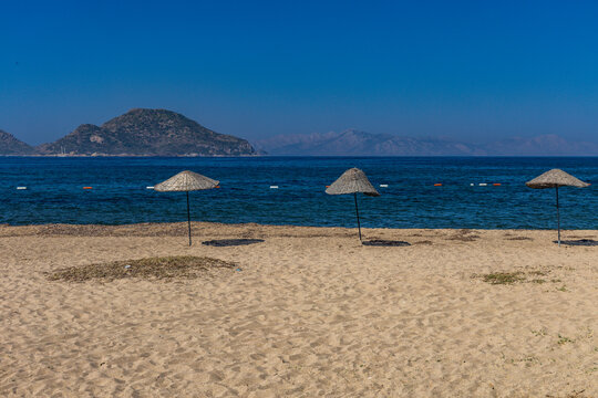 Empty sandy beach in Turgutreis near Bodrum, Turkey, with traditional straw umbrellas providing shade from the sun along the shores of the Aegean Sea.