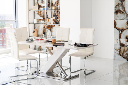 Empty modern conference room with white table and chairs. Workplace setup with notebooks, headphones and stationery