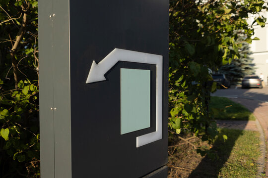 Parking exit sign. Black sign with white arrow indicating exit from parking area. Foliage and road in background. Close-up