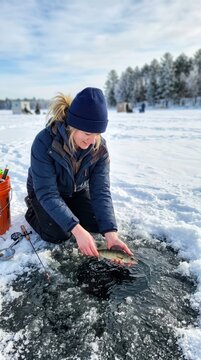 Joyful woman delicately holding her freshly caught fish beside a frozen hole on a glistening snowy lake