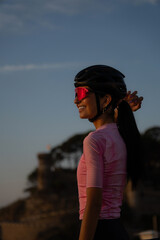 Profile portrait of a smiling, happy female cyclist adjusting her helmet, with the warm light of sunrise illuminating her face in Tossa de Mar. © sirbouman