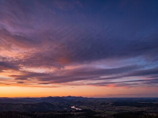 Fototapeta premium Panoramic Sunset over Mountain Valley and Winding River Under Dramatic Purple Sky
