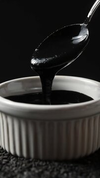 Glossy black sesame paste in bowl slowly rotates as spoon lifts and pours thick texture close up.