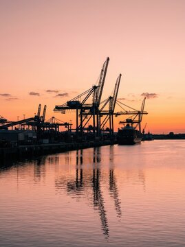 Silhouette of Container Cranes and Cargo Ship at a Busy Industrial Port During a Vibrant Sunset