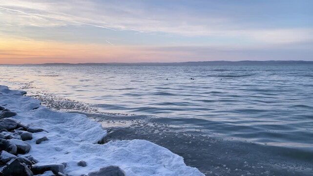 Winter sunset over Lake Balaton with icy snowy shore and calm water in Hungary
