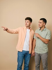 Obraz premium Two Young Men Pointing and Looking Away in Surprise Against a Neutral Studio Background