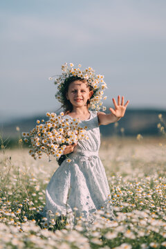 Young girl waving hand while holding bunch of Matricaria chamomilla flowers in a sunny meadow