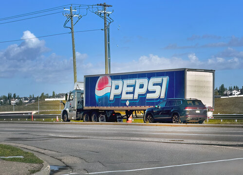 Calgary, Alberta, Canada. Sep 10, 2026. Side view of semi trailer truck with prominent Pepsi logo parked along suburban highway under blue sky.