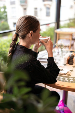 Young woman drinking coffee during break in bright cafe setting while sitting alone at table