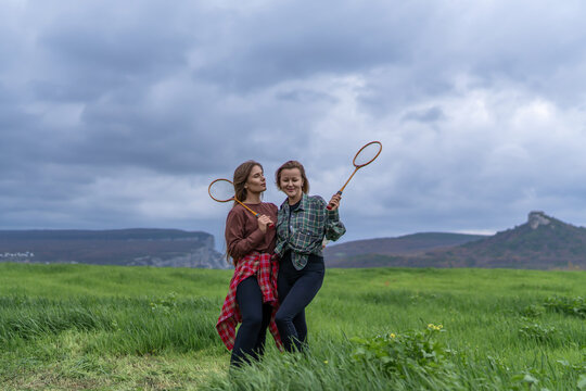 Friends posing with vintage badminton rackets in a green meadow landscape under a cloudy sky during an outdoor leisure activity