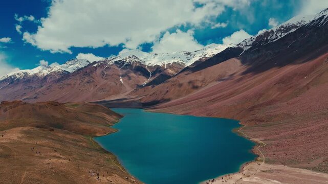 cinematic aerial drone shot of stunning chandratal lake in spiti valley, himachal pradesh. The crystal blue lake is surrounded by rugged himalayan mountains and dramatic high altitude landscape.