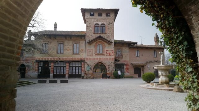 Visitor walks into a quiet Grazzano Visconti courtyard framed by an arch, revealing the neo-medieval palace and central fountain.