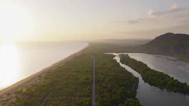 Aerial dolly along road separating Kaiafas Lake from Ionian Sea coast at sunset, symmetrical balance with soft haze glow