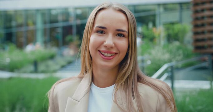 Portrait of beautiful young female entrepreneur standing in city street. Confident woman with blond hair posing outdoors with laptop in his hands