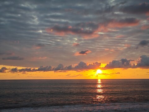 Ocean sunset with rolling waves and golden reflection. Bright sun on the horizon under cloudy sky