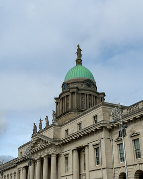 The Custom House in Dublin features a green copper dome, classical columns, statues and ornate stonework beneath a cloudy Irish sky.