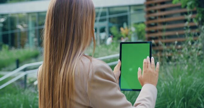 Back view woman hands touching green screen digital tablet outdoor. Unrecognizable girl using mock up phone