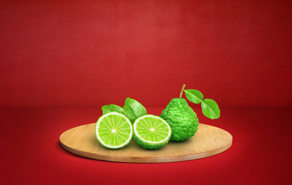Fresh kaffir lime with slices on wooden board over red background.