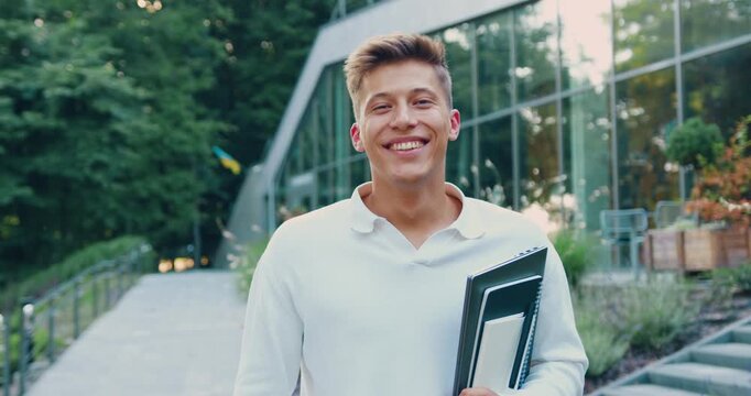 Portrait of young male entrepreneur standing in city street. Confident man with blond hair posing outdoors with laptop in his hands