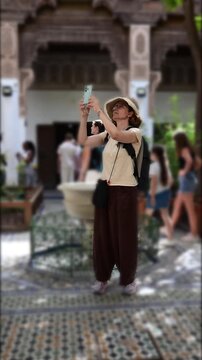 Marrakech, morocco. August 10, 2026. Female traveler with a backpack filming with a smartphone in a traditional moroccan courtyard with mosaic tiles, enjoying her vacation