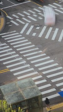 Pedestrians walk across a crosswalk in a busy city intersection with vehicles and urban elements in view. Time-lapse, Seoul, South Korea