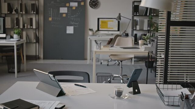 Empty modern open plan office space showing desks with computers, digital tablet, smartphone, and notes. Footage suitable for corporate presentations and business marketing