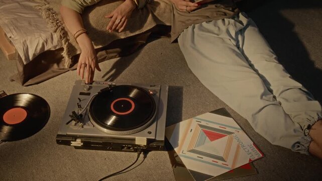 Young Caucasian couple playing vinyl record on turntable, cuddling and talking affectionately in bedroom. Footage suited for romantic lifestyle ads and retro music streaming campaigns
