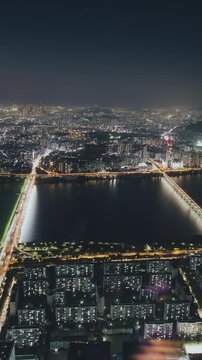 Aerial perspective of a lively city at night, showcasing illuminated buildings and a river reflecting the vibrant lights. Time-lapse, Seoul, South Korea