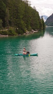 A Woman Sits On Stand-up Paddleboard With Dogs Paddling On Lake Achensee In Tyrol, Austria. Vertical, Aerial Shot